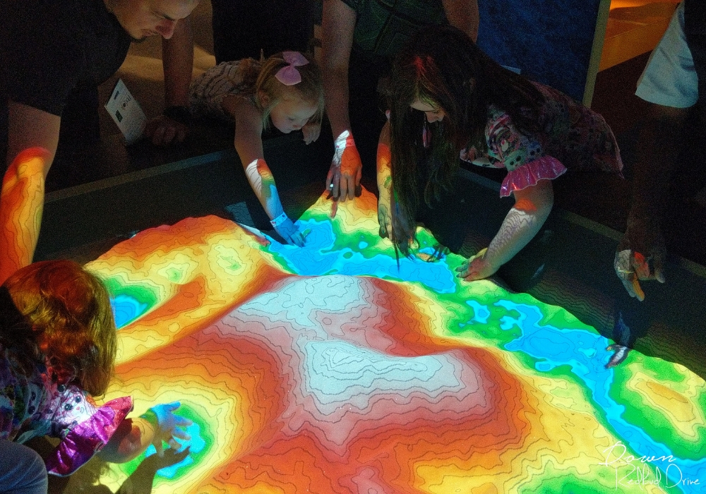 kids playing with an interactive topographical map inside the perot museum of nature and science
