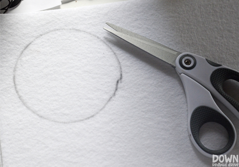 diy-dryer-vent-snowman-wide-3 A circle drawn on a piece of white felt with a pair of scissors sitting on it.