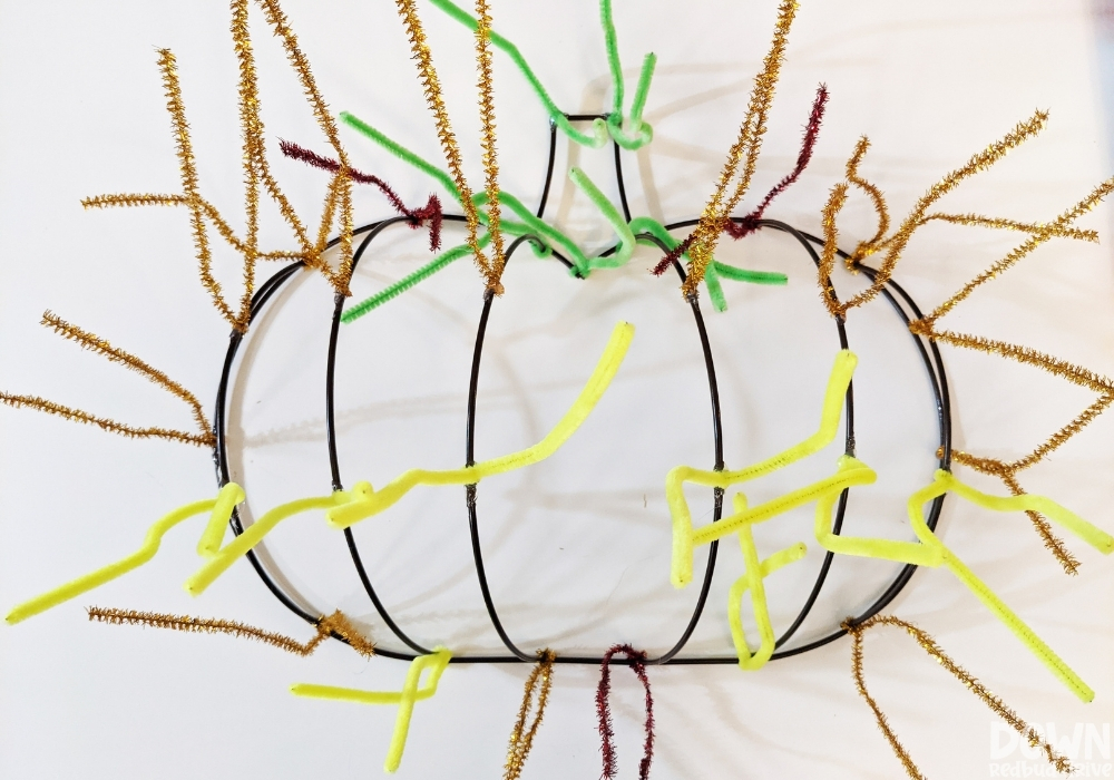diy-mesh-pumpkin-wreath-wide-2 Gold, green and yellow pipe cleaners attached to a pumpkin wreath shape.