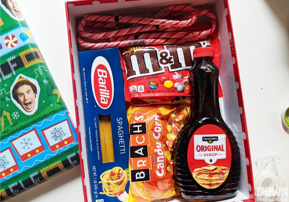 elf-food-groups-gift-idea-wide-4 An elf decorated gift box with candy canes, peanut butter M&Ms, spaghetti, candy corn and syrup in it.