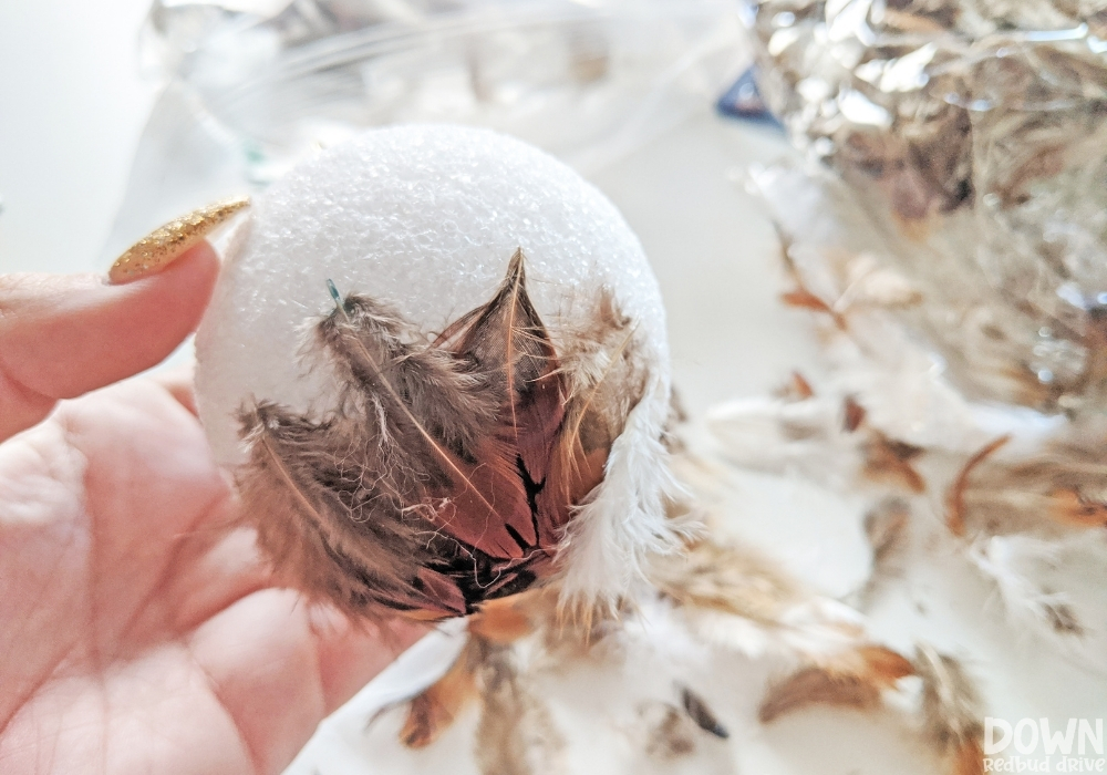 feather-ornament-diy-wide-4 Up close picture of feathers being attached to a foam ball for the feather ornament DIY.