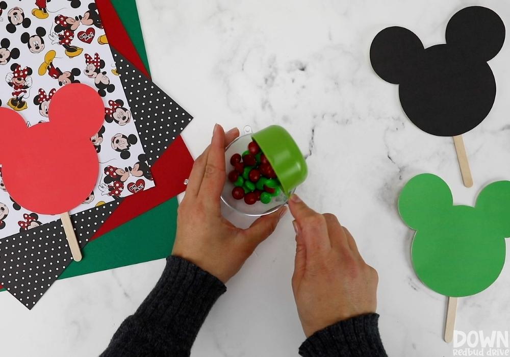 mickey-and-minnie-christmas-pops-wide-4-1 M&Ms being added to a plastic dome for the Mickey and Minnie Christmas Pops.