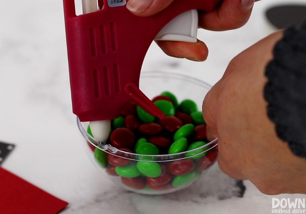 mickey-and-minnie-christmas-pops-wide-4-2 Glue being added to a plastic dome full of M&Ms to add a printable to.