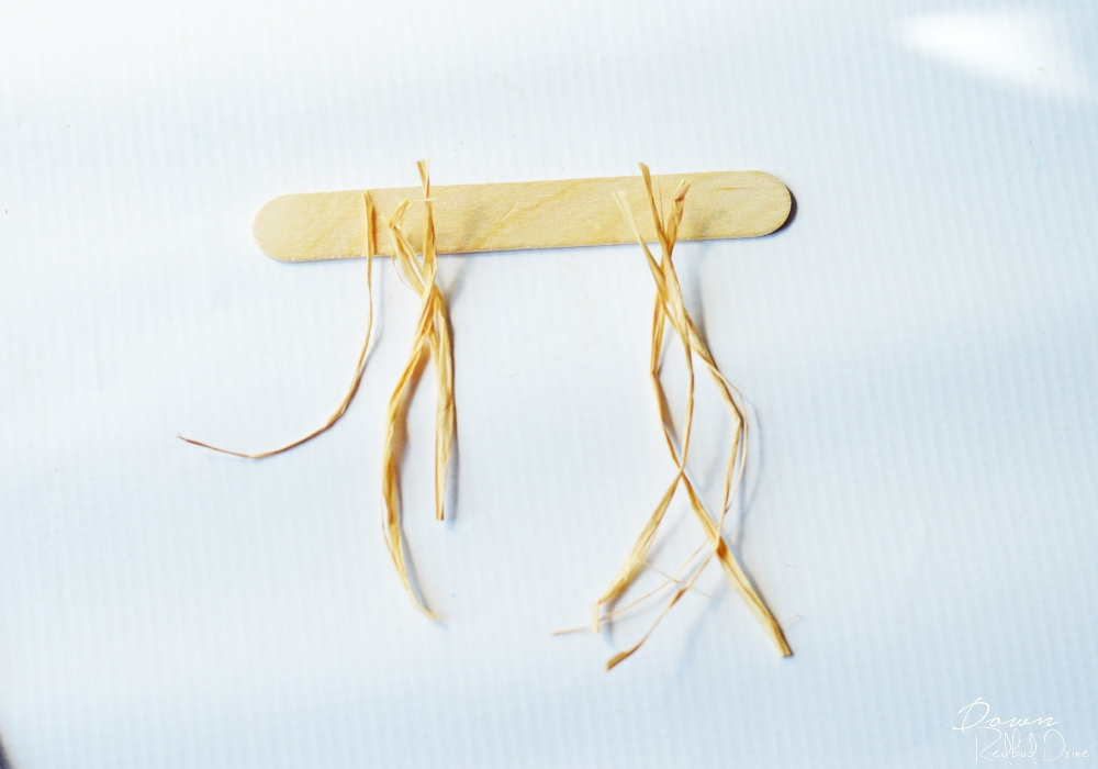 popsicle-stick-scarecrow-2 little pieces of raffia on a popsicle stick with a white background