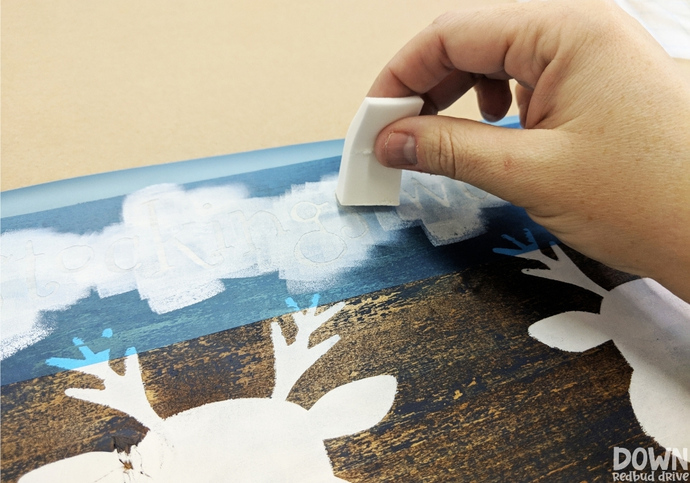 reindeer-stocking-holder-diy-wide-4 A hand painting white paint onto a stencil.