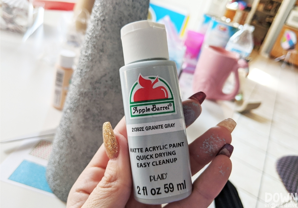 sea-glass-christmas-tree-diy-wide-2 A bottle of gray acrylic paint in front of a foam cone that has been painted gray.