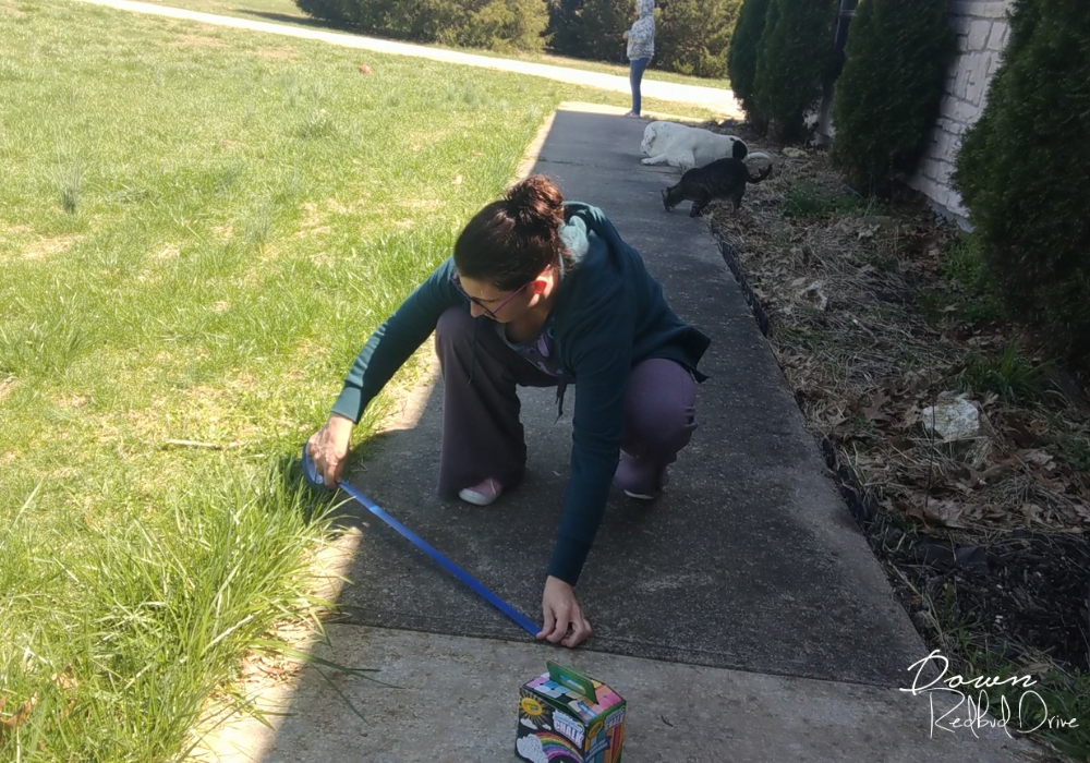 sidewalk-chalk-mosaic-2 woman putting a strip of painter's tape on a sidewalk outside on a sunny day